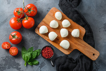 Wall Mural - Mini balls of mozzarella cheese, on chop wood board ingredients for salad Caprese. over grey background. Top view