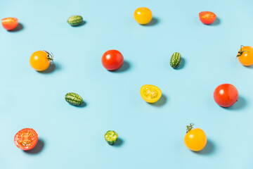 Colorful food pattern of mini cucumbers and yellow and red tomatoes on blue background