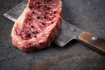 Wall Mural - Juicy Raw new York beef steak and a butcher's hatchet close up on a dark background, close up