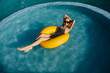 © Bostan Natalia - Young woman wearing one-piece swimsuit, swimming in a pool, lying on a bright yellow swim ring.