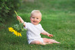 Little baby sitting and holding sunflower in the garden, baby sitting on green grass and smiling