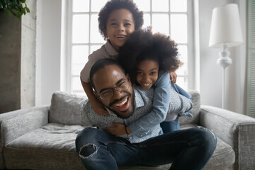 Portrait of overjoyed young playful african American father have fun in living room with two small ethnic children, excited biracial dad play with little kids, engaged in funny activity together