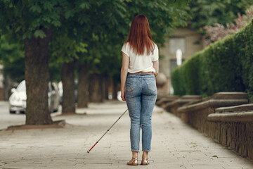 Wall Mural - Blind woman is walking on the sidewalk in city. Woman using a white cane.