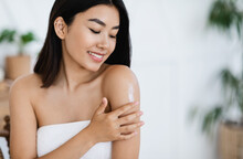 Smiling Asian Girl Applying Body Lotion On Her Shoulder