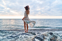 Boho Chic Woman In Long Fluttering Dress And Felt Hat Standing Back On Stone By The Sea