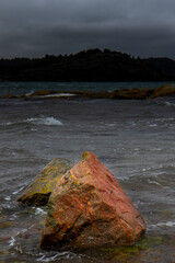 View of two reddish rocks on the shore with a sea background