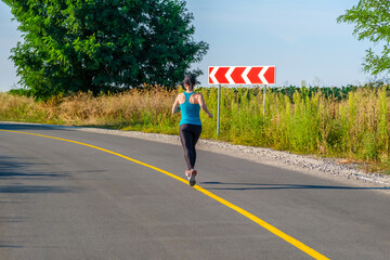 young fitness white woman running up to turn country road.