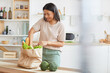 © Seventyfour - Waist up portrait of elegant mixed-race woman unpacking bags with food while standing in white kitchen interior and smiling, food delivery service, copy space