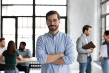 Head Shot Portrait Smiling Confident Businessman Wearing Glasses Standing In Modern Office Room With Arms Crossed, Diverse Colleagues On Background, Executive Boss Startup Founder Looking At Camera