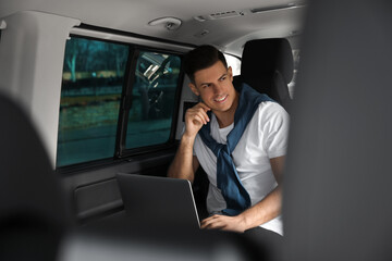 Handsome man working with laptop on backseat of modern car