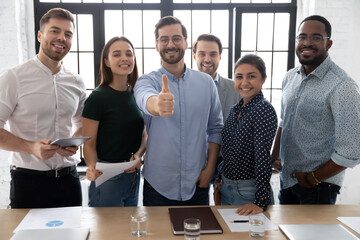 Smiling executive showing thumb up, standing with diverse employees team in modern office room, looking at camera, smiling businessman recommending corporate service, good career, human resources