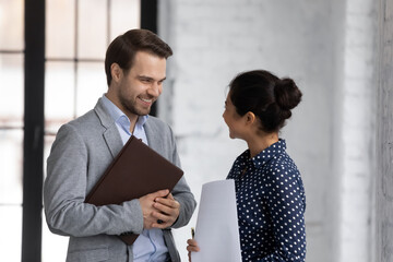 two diverse employees standing in modern office, discussing project, smiling businessman and indian 