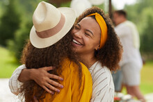 Portrait Of Young African-American Woman Hugging Friend And Smiling Cheerfully While Enjoying Outdoor Party In Summer