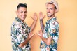 © Krakenimages.com - Young gay couple of two men wearing summer hat and hawaiian shirt inviting to enter smiling natural with open hand