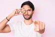 © Krakenimages.com - Handsome hispanic man holding cookie pointing with finger to the camera and to you, confident gesture looking serious