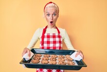 Young Blonde Woman Wearing Baker Uniform Holding Homemade Cookies Afraid And Shocked With Surprise And Amazed Expression, Fear And Excited Face.