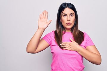 Young beautiful brunette woman wearing casual pink t-shirt standing over white background Swearing with hand on chest and open palm, making a loyalty promise oath