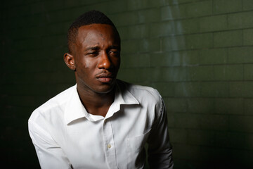 Wall Mural - Young African businessman against brick wall in the dark