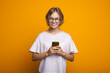 © Strelciuc - Blonde woman with eyeglasses chatting on mobile and smile on a yellow studio wall wearing a white t-shirt