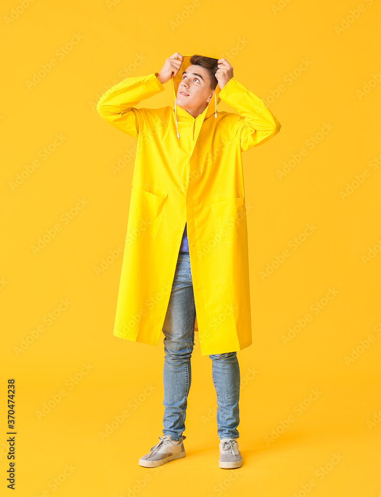 Handsome young man in raincoat on color background