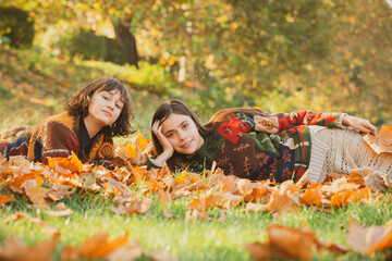 Wall Mural - Girls lying on leaves. Portrait of Two beautiful happy smiling young women lying in autumn leaves and having good time on the outdoors background.