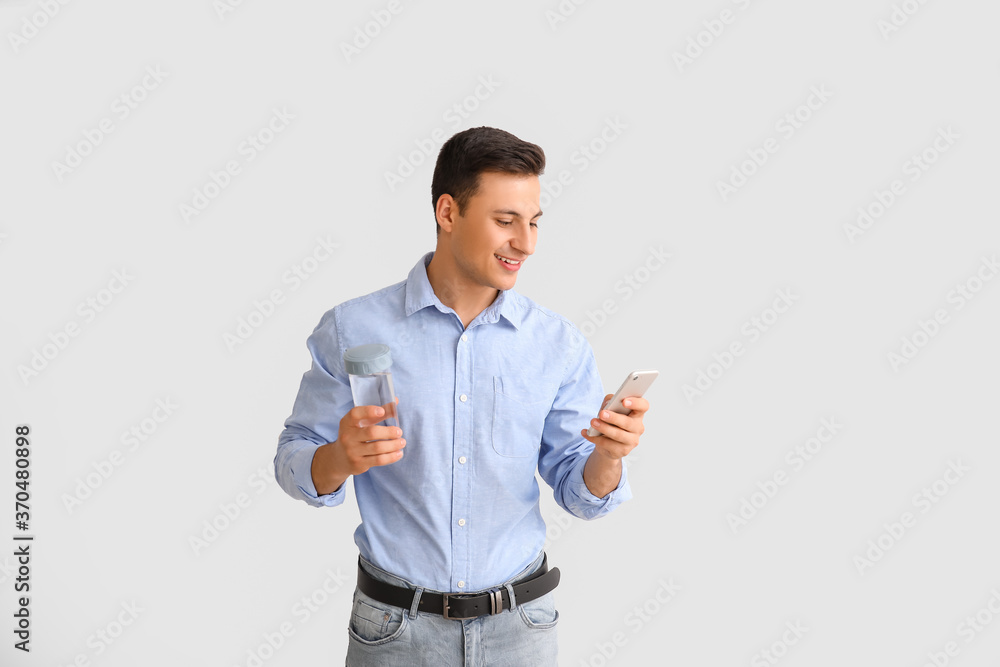 Young man with bottle of water and phone on light background