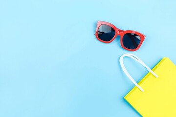 Wall Mural - yellow paper shopping bag and red sunglasses on blue background with copy space