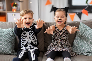 Poster - halloween, holiday and childhood concept - smiling little boy and girl in costumes having fun at home