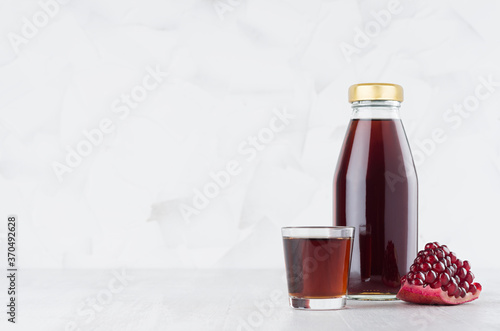 Bright red pomegranate juice in glass bottle mock up with wine glass, fruit grains on white wood table in light interior, template for packaging, advertising, design, branding product.