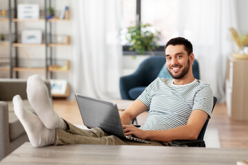 Wall Mural - technology, remote job and lifestyle concept - happy smiling man with laptop computer resting feet o