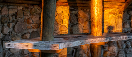 Wall Mural - wooden table against the background of a stone wall illuminated by the warm natural light of the setting sun