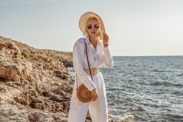 outdoor summer fashion portrait of elegant woman wearing white linen suit, belt, straw hat, sunglass