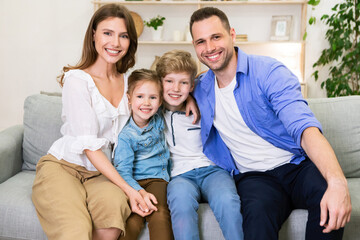 Wall Mural - Family Hugging Sitting Together On Couch Smiling To Camera Indoor