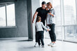 © standret - Woman in formal clothes and with camera in hand standing inside of empty room with man and little boy that running and having fun