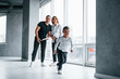 © standret - Woman in formal clothes and with camera in hand standing inside of empty room with man and little boy that running and having fun