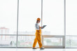 © standret - Near big window. Female worker or engineer in yellow uniform and hard hat standing indoors