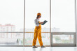 © standret - Near big window. Female worker or engineer in yellow uniform and hard hat standing indoors