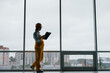 © standret - Near big window. Female worker or engineer in yellow uniform and hard hat standing indoors