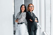 © standret - Two business women standing together indoors in the office near big window