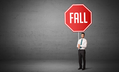 Young business person holding road sign with FALL inscription, new rules concept