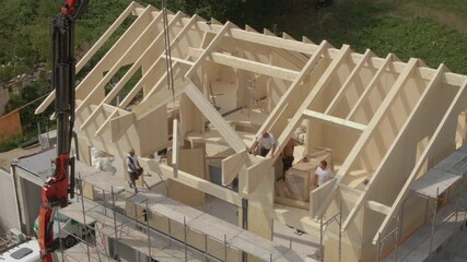 Wall Mural - DRONE: Flying near a modern prefabricated house being built in the Slovenian countryside. Group of contractors mounts a wooden arch on the roof of a cross-laminated timber house under construction.