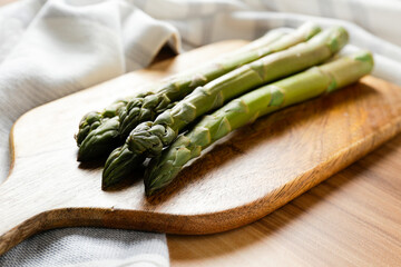 Wall Mural - Bunch of raw asparagus stems on wood textured table. Edible Asparagus Officinalis sprouts laid on bamboo cutting board. Close up, copy space, top view, flat lay, background.