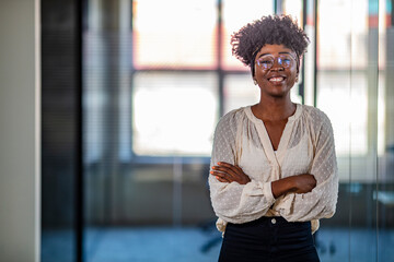 Wall Mural - Portrait of a professional businesswoman standing in an office. Beautiful smiling curly-haired businesswoman. Portrait of a young businesswoman standing with her arms crossed in an office