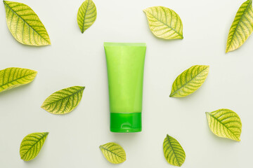 Natural herbal skincare products mock up. Top view of green squeeze bottle plastic tube with fresh leaves on green background. Packaging of lotion, cream, facial foam, gel, soap or shampoo.