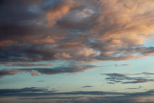 Blue bright sky with orange and pink clouds, natural beautiful background. Soft sunset or sunrise daylight. Stock photo with empty space for text and design. 