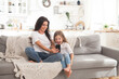 © Алина Троева - Attractive young mom and little daughter playing online games at home using smartphone, having video chat or watching movie. Distance education. Video conference or virtual event on quarantine.