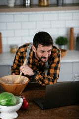 Wall Mural - Portrait of handsome man in kitchen. Young man cooking while having video call.