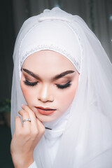 Wall Mural - Portrait of a beautiful asian muslim bride with make up in white wedding dress and hijab headscarf, natural light.