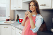 © fotofabrika - Pretty young woman in red apron enjoying a cup of coffee in her kitchen