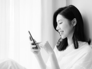 Wall Mural - Young asian woman using smartphone at home in black and white